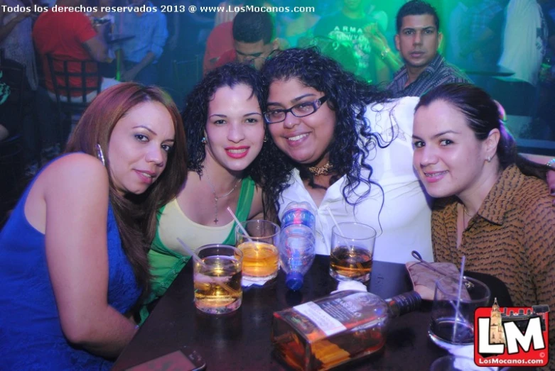 four women smiling for the camera, one drinking a drink and one taking a picture of themselves