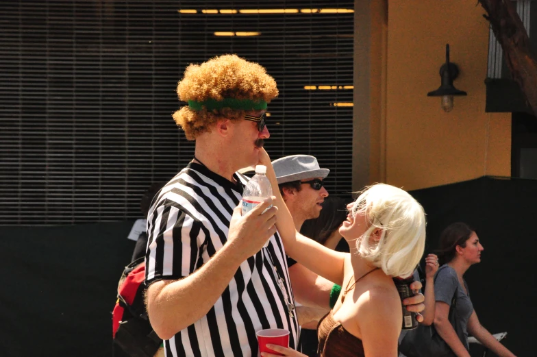 woman in a referee suit giving a drink to a man in drag suit