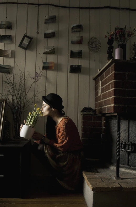 a woman with flowers in her hand is sitting near a fireplace