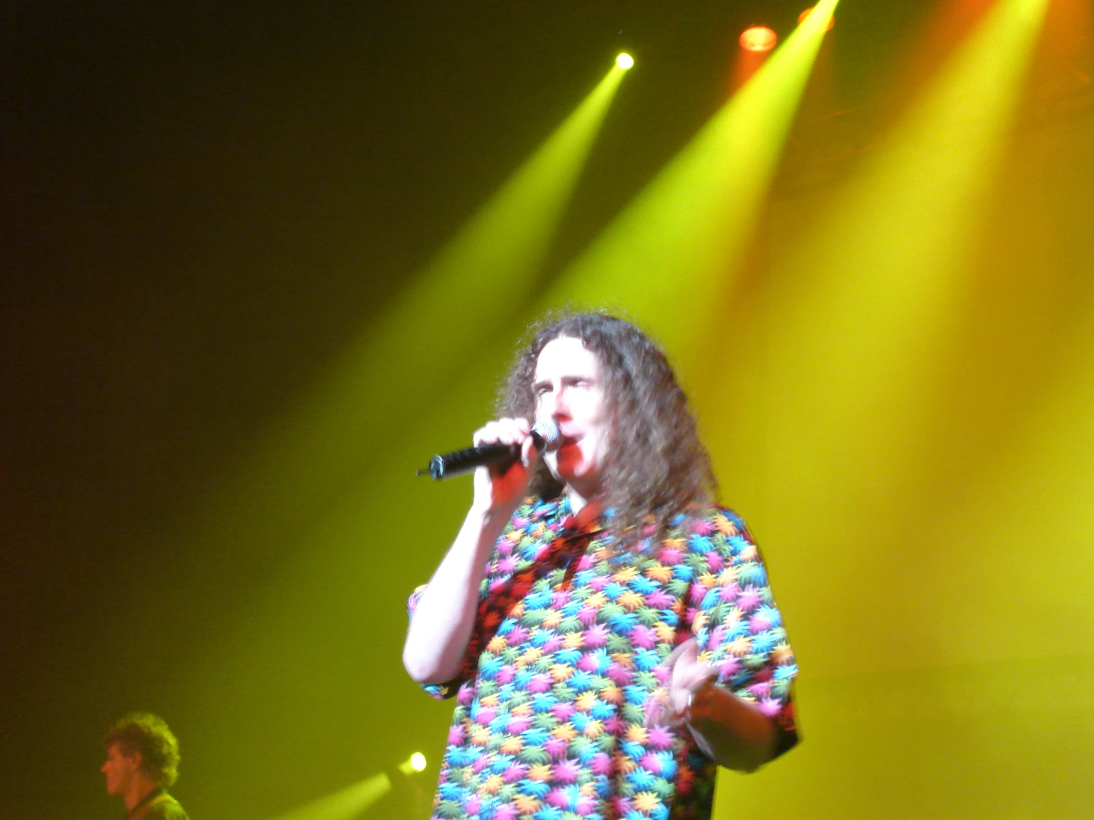 a singer with long hair and a colorful shirt performs on stage