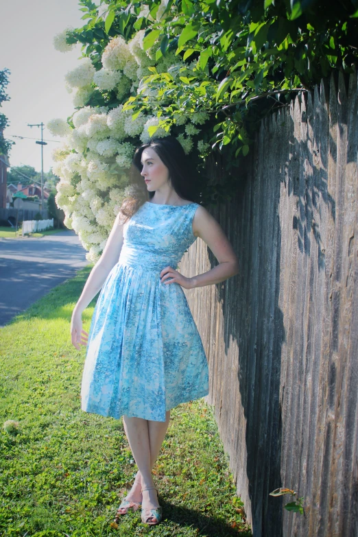 a woman wearing blue dress leaning against a fence