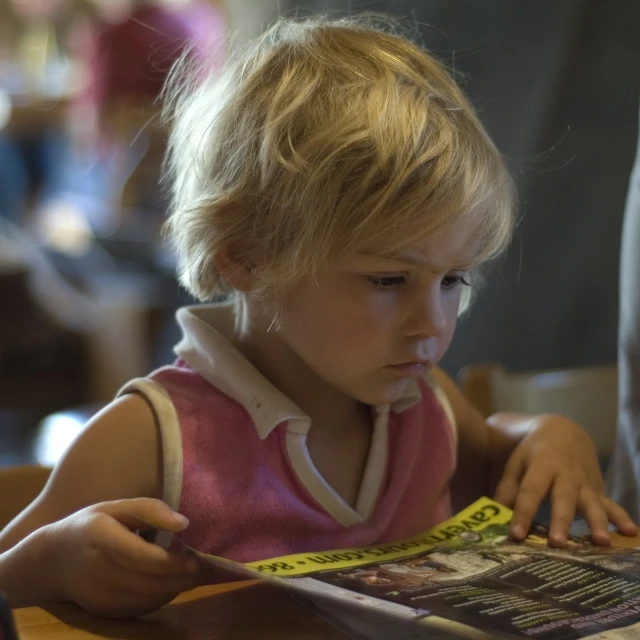 a girl sitting at a table reading a magazine