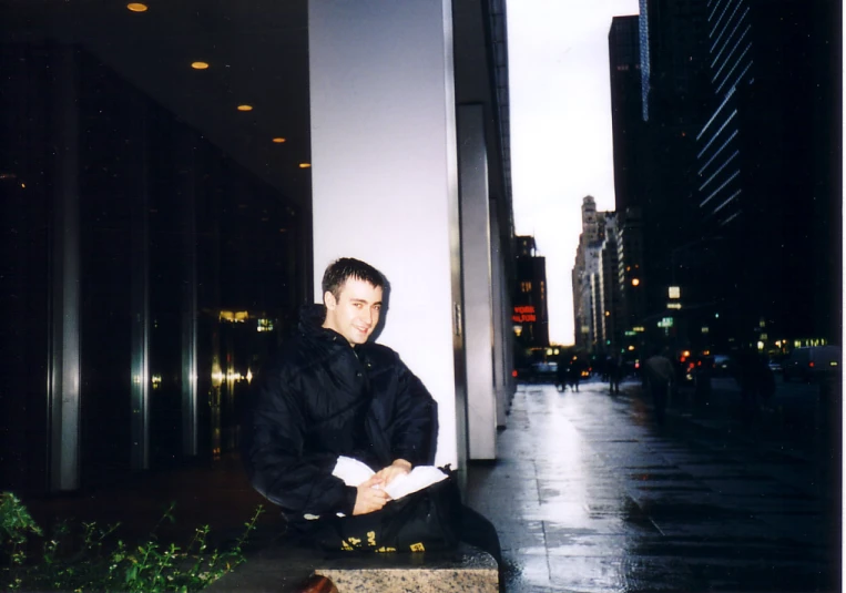 a man is sitting on the side walk in the rain