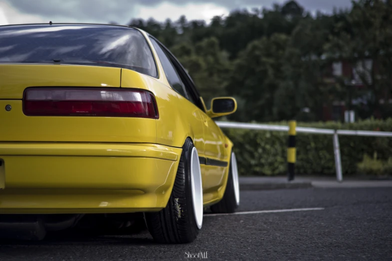 a yellow car parked by a fence with trees in the background