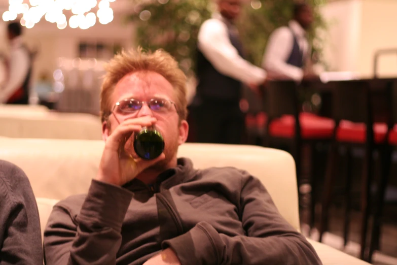 a man sitting on a couch holding a green bottle