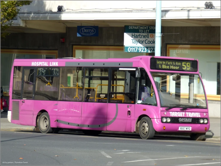 a pink city bus parked in front of a parking lot