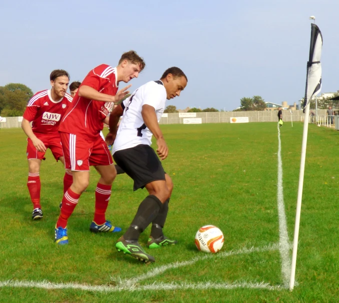 three young men kicking a soccer ball across a field