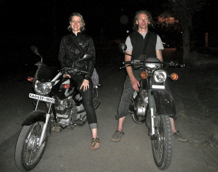 a couple of people standing next to a motorcycle at night