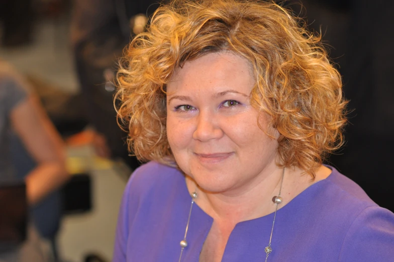 a smiling woman wearing a purple shirt and necklace