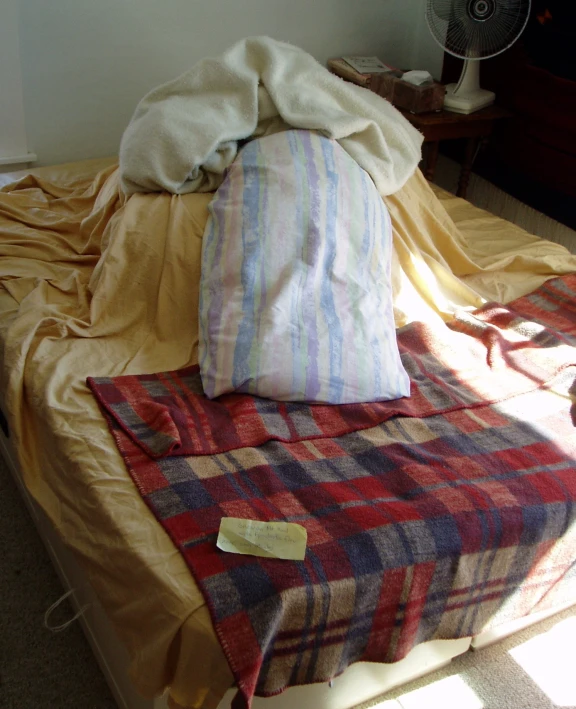 bed with yellow sheets and a red blue plaid blanket