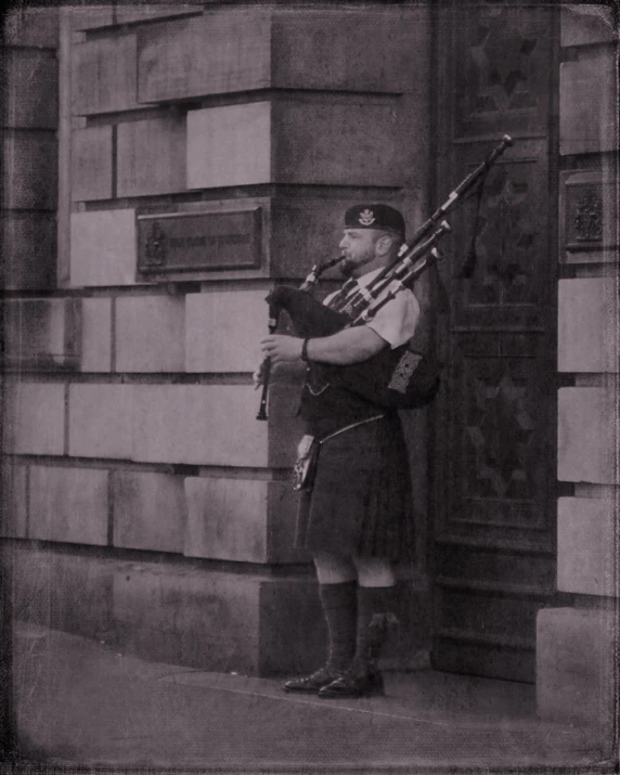 a person standing outside of a building while playing the bagpipe