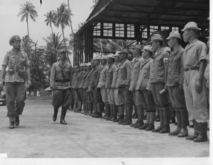 an older black and white po shows a man in a uniform standing by a large group of soldiers