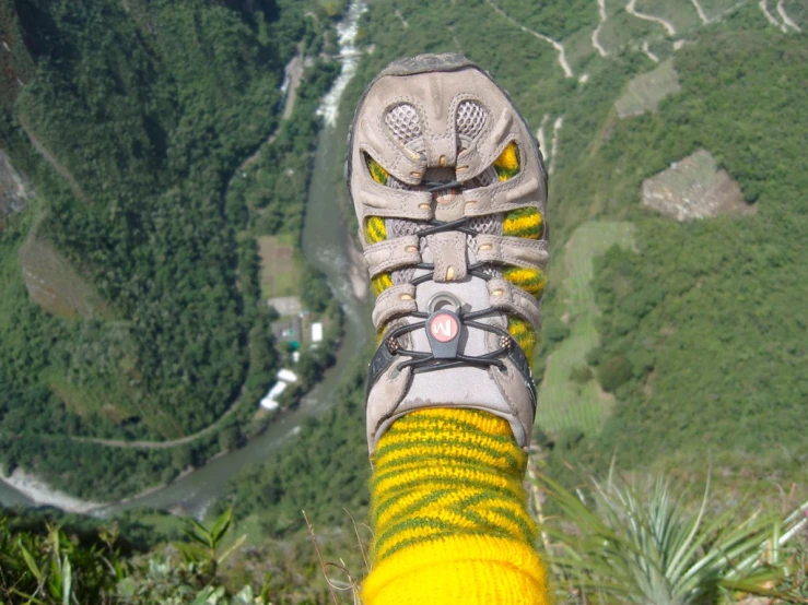 person in yellow socks and shoes looking down at a mountain valley