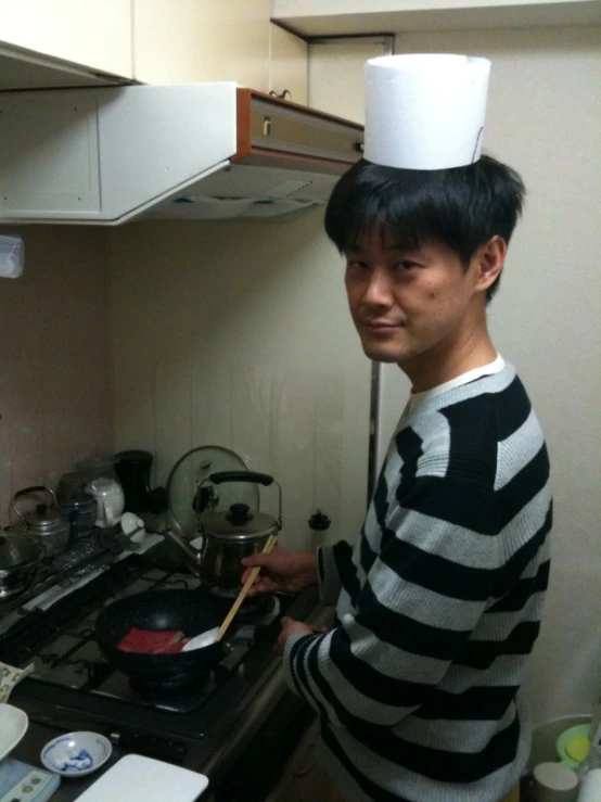 a young man in the kitchen wearing an odd looking hat