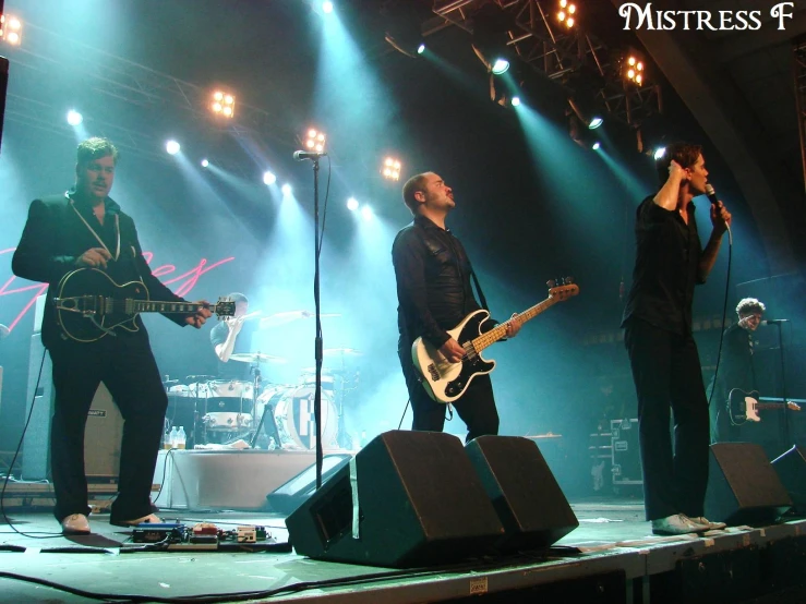 five men on stage with microphones and a guitar