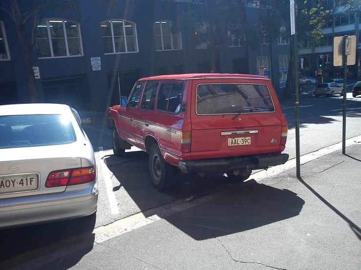 a small red station wagon parked at the curb of a city street