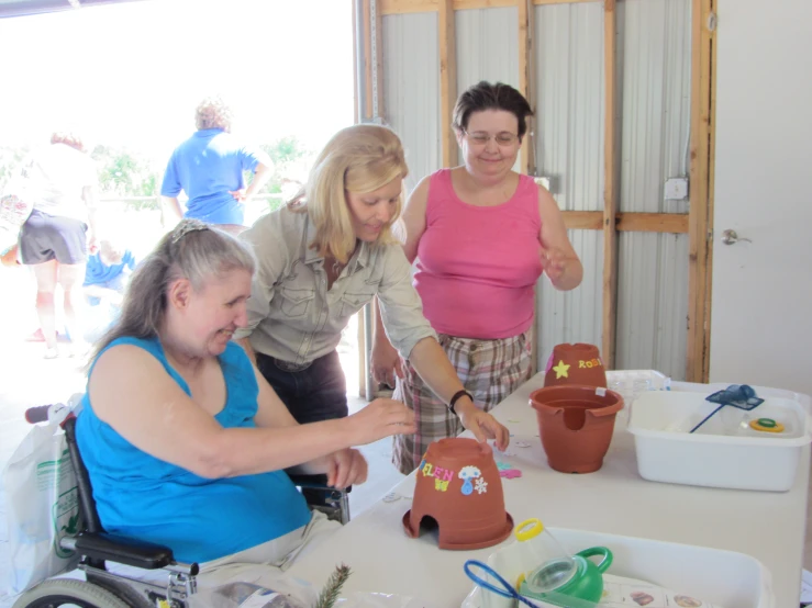 three woman are decorating a flower pot in the center of a table