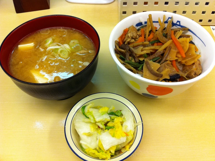 a bowl of soup, a bowl with a salad, and a bowl of noodles