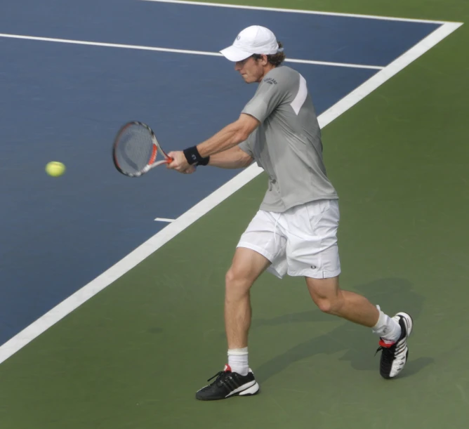 a man in a gray shirt and white shorts playing tennis