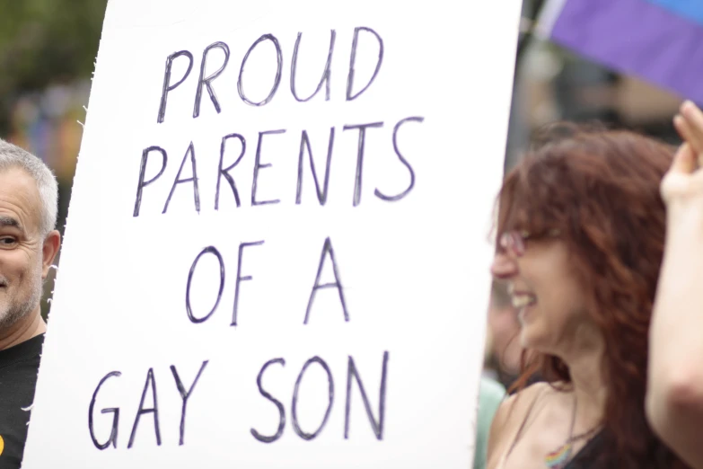 man holding up sign during pride parade in front of spectators