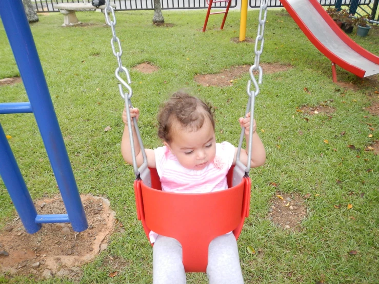 a baby sitting in a red swing next to a green field