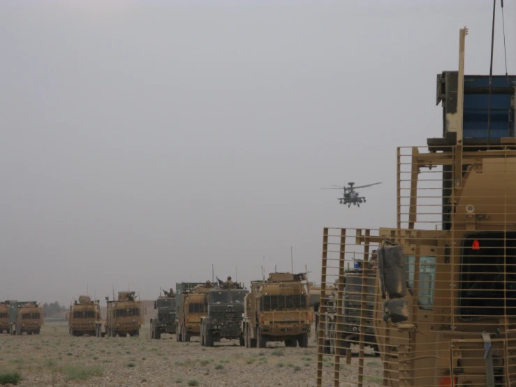 helicopter flying over the army vehicles on the road