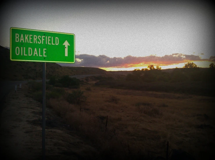 green and white road sign with sunset in background