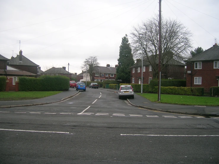 cars are driving on a suburban street with houses in the background