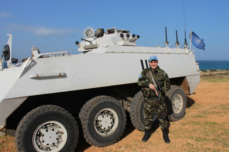 a man dressed in camouflage poses next to an army vehicle