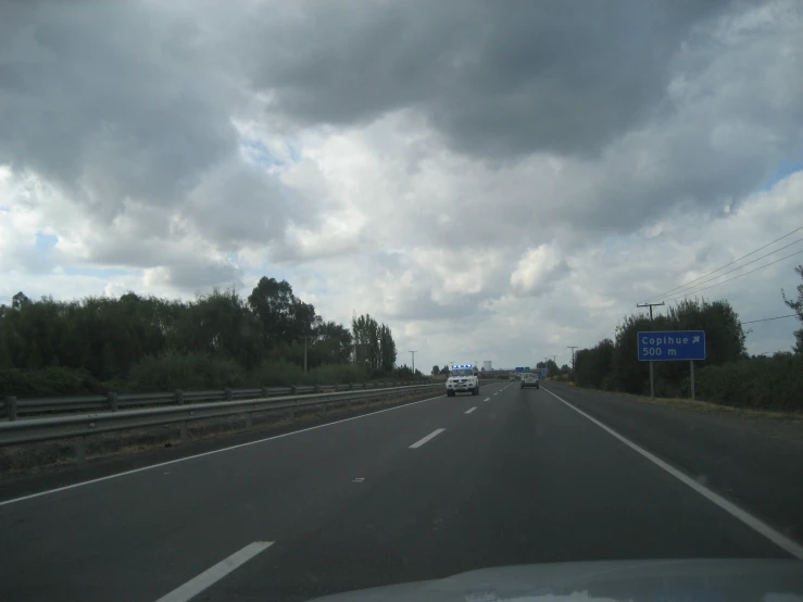 clouds hover above a car going down an empty highway