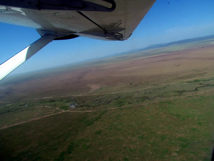 the wing of an airplane flying over grass and a plain