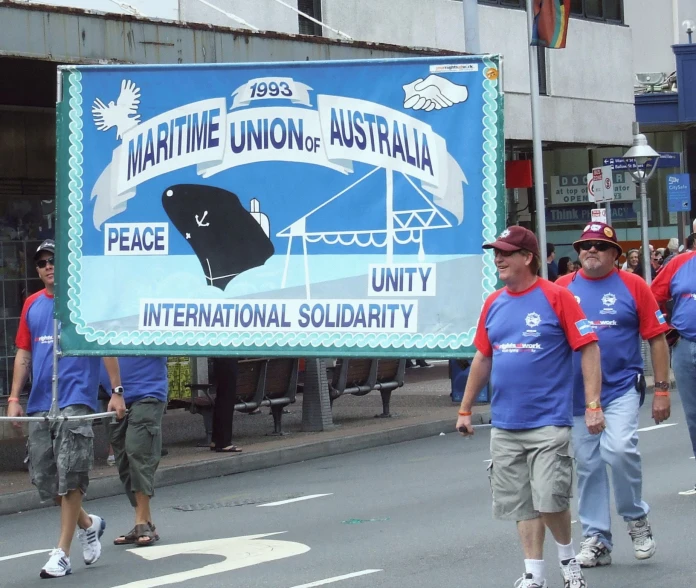 two men walk behind an opposing banner of a large boat