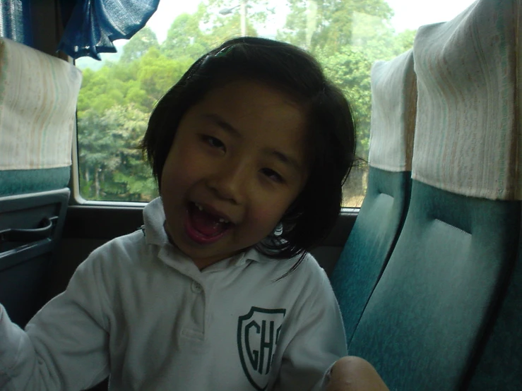a little girl in a school uniform making a silly face while sitting in a car