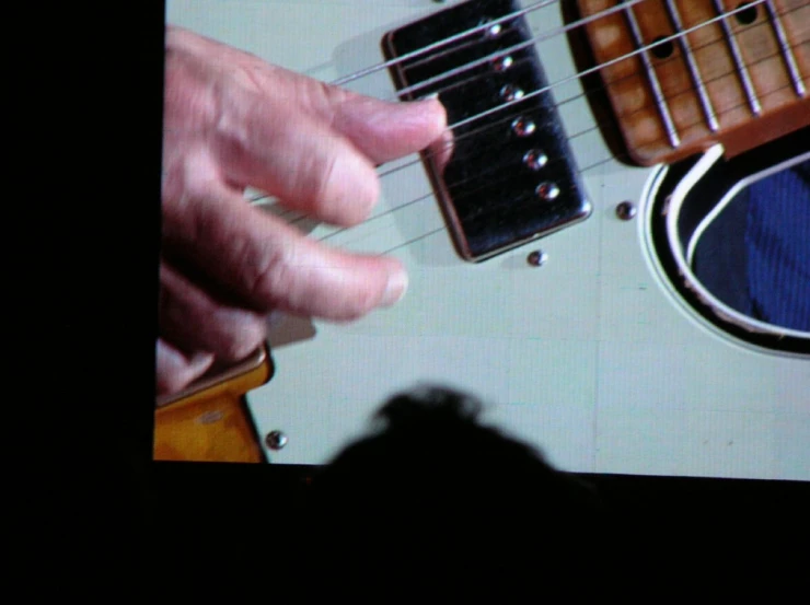 hand playing an electric guitar with strings while someone is watching