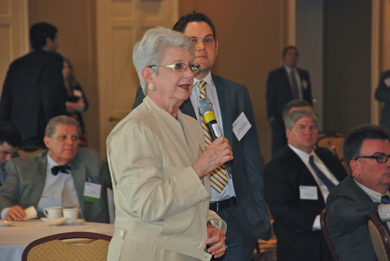 an older woman with glasses is speaking to an audience