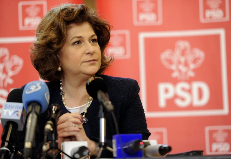 woman in black jacket standing behind microphones and making a speech