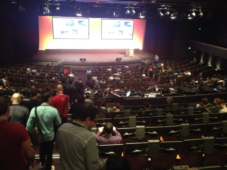 a crowd of people sitting in an auditorium with two big screens