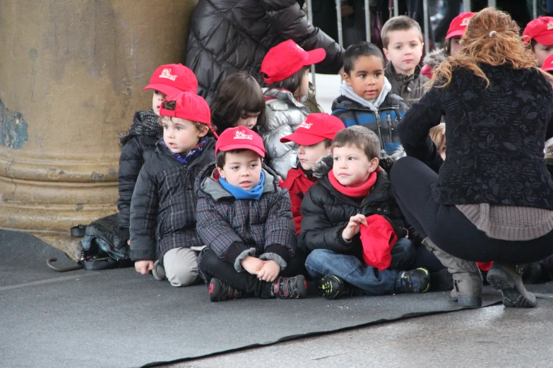 several children in red hats are sitting on the sidewalk