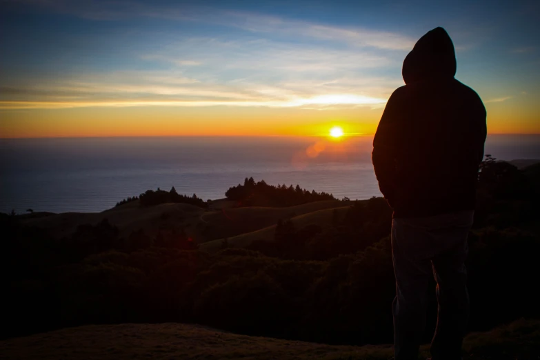 the person in a black jacket is looking at a sunset