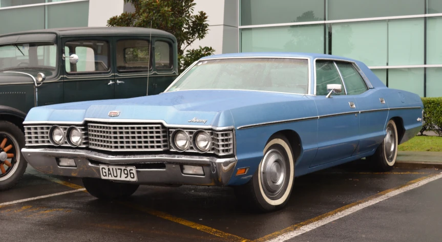 an older blue car sits parked near a classic black truck