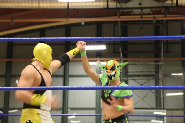 two people standing in a ring one wearing an evil mask and the other in costume holding hands with another man