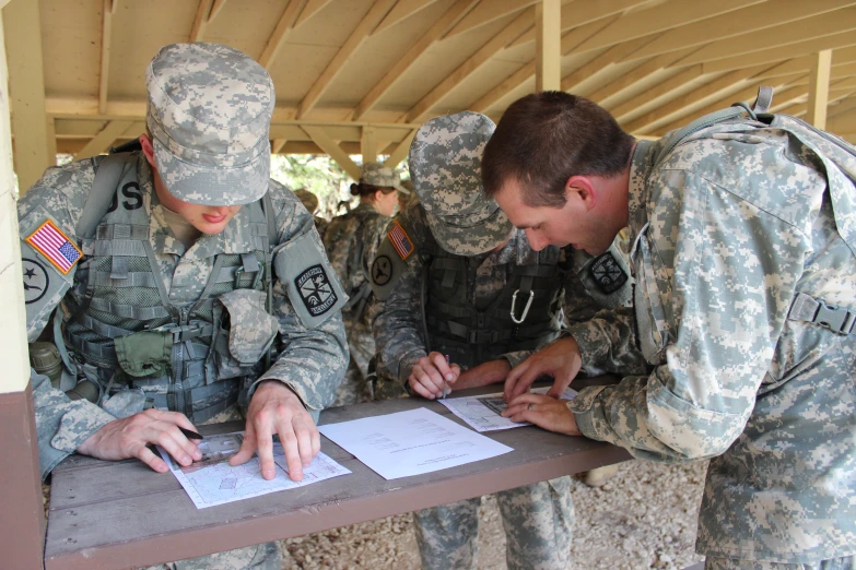 three soldiers in uniforms sitting at a table signing papers