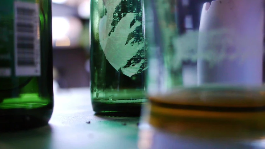 three green soda bottles on a table with another one behind it