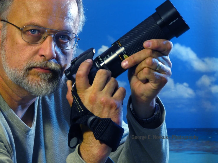 man holding a camera while standing in front of a blue sky