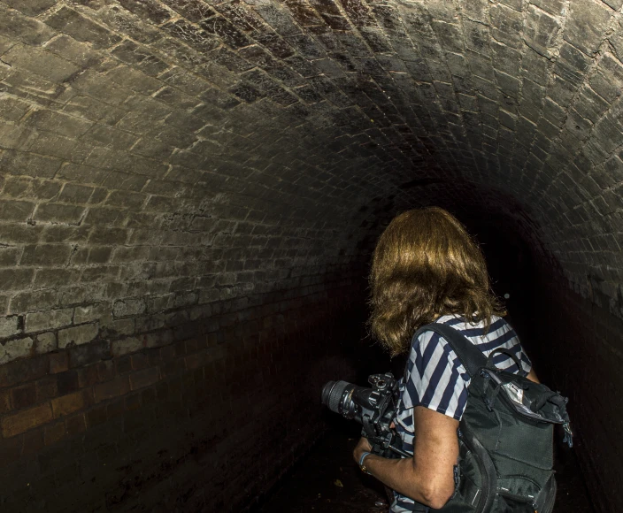 a woman wearing a backpack and backpack standing inside of a small tunnel