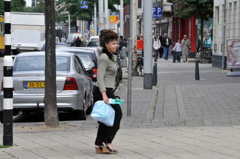 a woman carrying two bags walks down the sidewalk on her heels