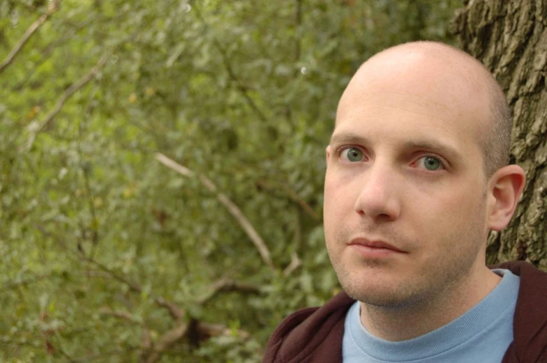 a bald man with his eyes closed, next to a tree