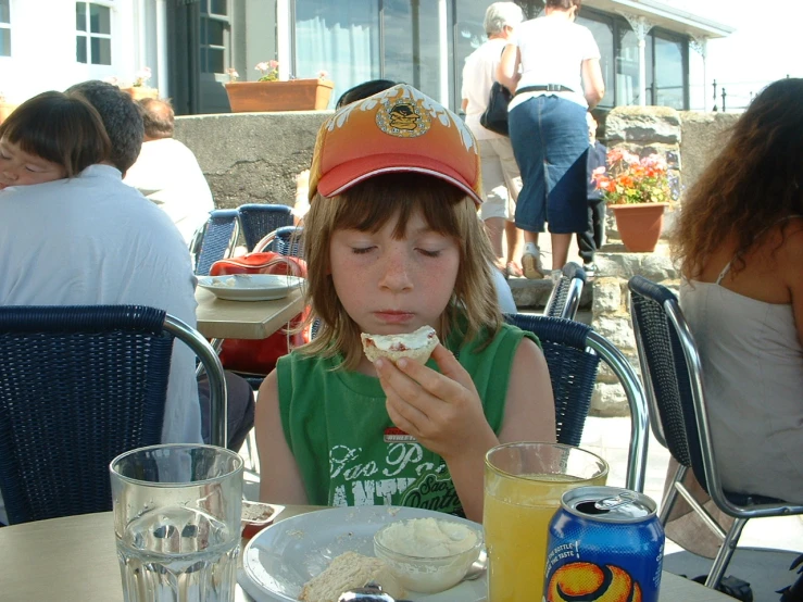 a little girl wearing an orange hat eats an ice cream sandwich at an outside dining area