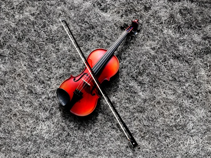 a red violin laying on the ground next to a pair of sticks