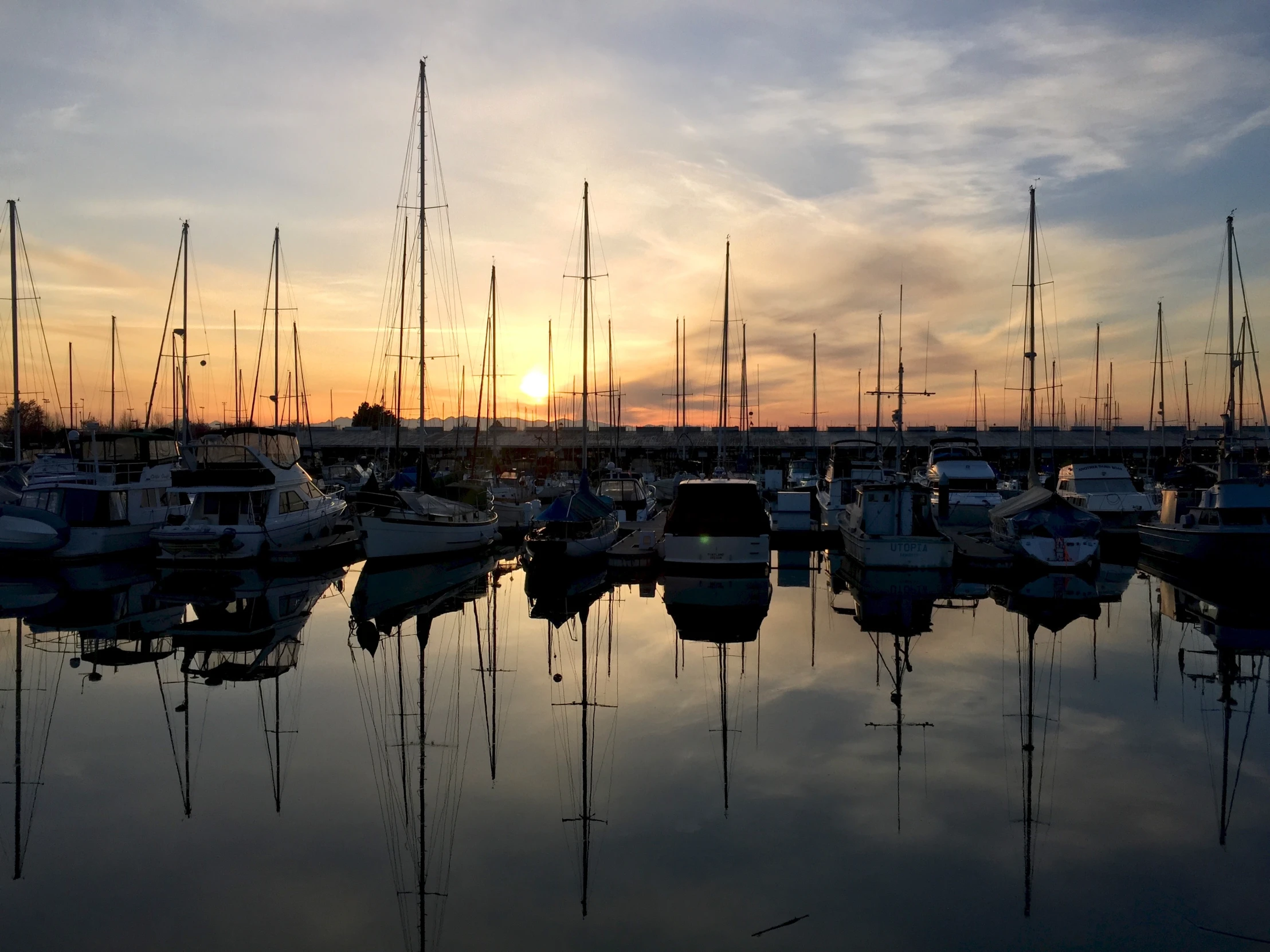 a marina with sailboats at sunset as it is reflected in water